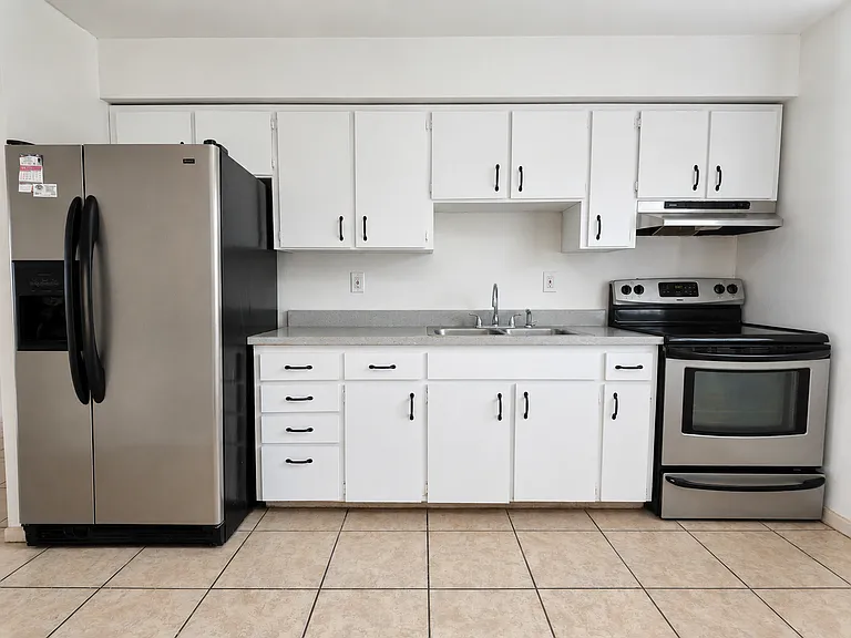 Kitchen with white cabinetry, refrigerator, oven, and tile flooring.